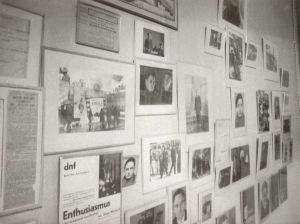 Wall in a room in Vertov's apartment, displaying framed photographs and articles